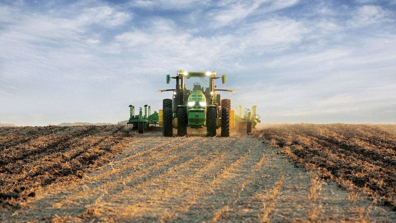 Tractor John Deere autonom care trage un echipament de arat pe un teren deschis.