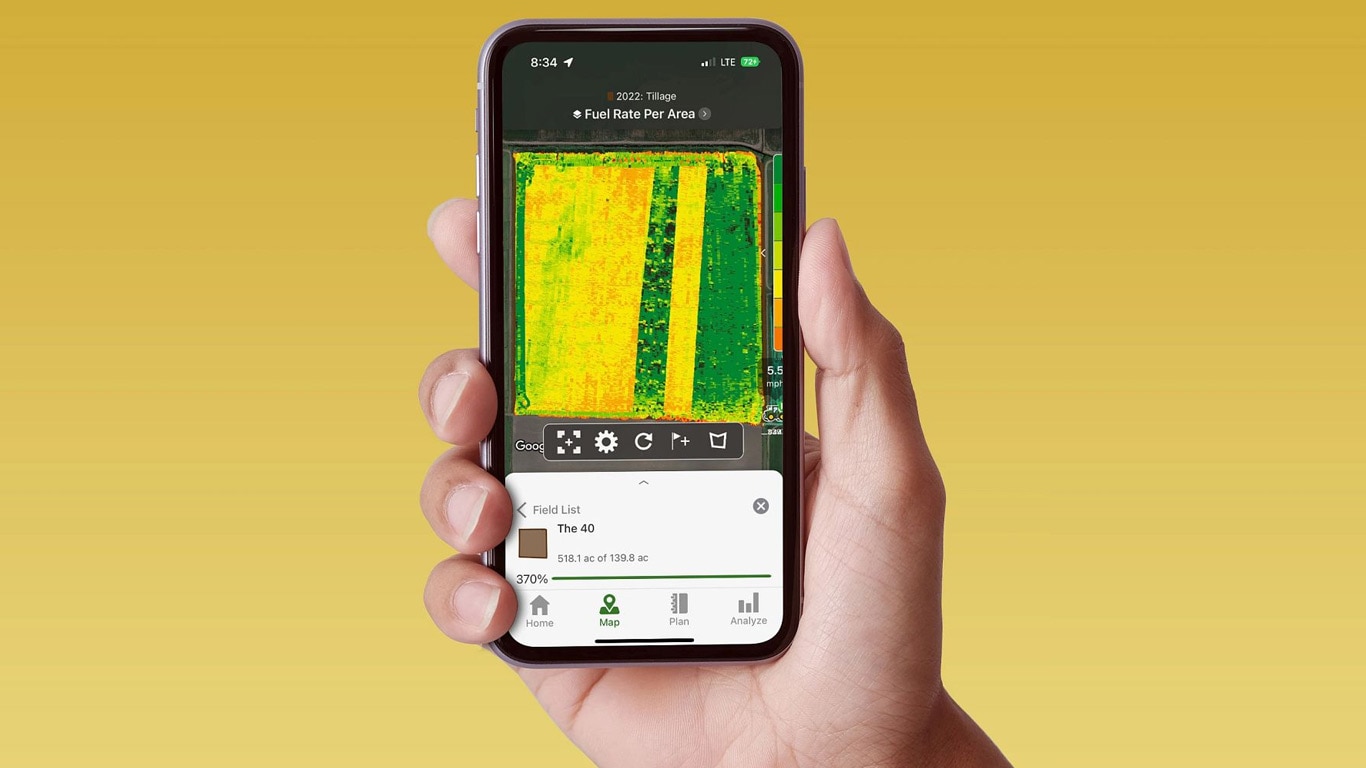 O mână ţinând un smartphone care afişează un ecran John Deere Operations Center cu date privind consumul de carburant.