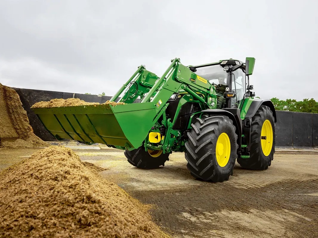 Cupa încărcătorului frontal este umplută cu furaje pe un tractor John Deere în timpul lucrărilor de manevrare a materialului.
