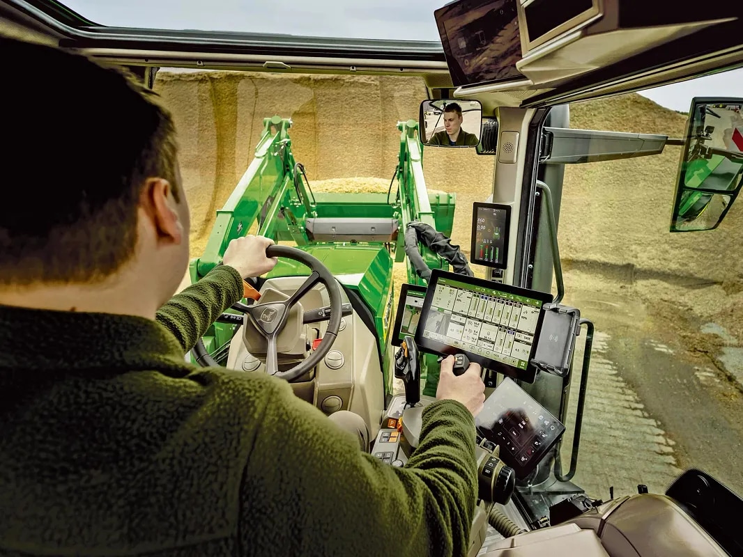 Vedere interioară a cabinei tractorului John Deere care prezintă comenzile operatorului şi operarea încărcătorului frontal.