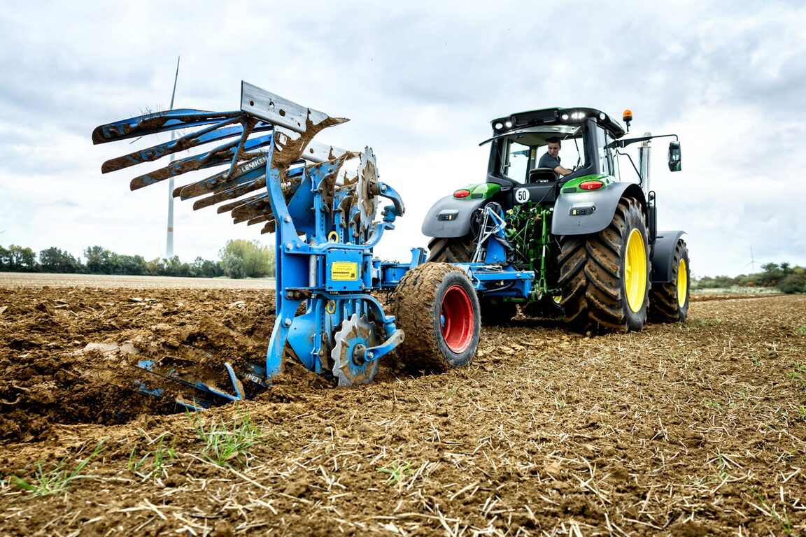 Un tractor John Deere ară cu un plug albastru reversibil pe un câmp recoltat