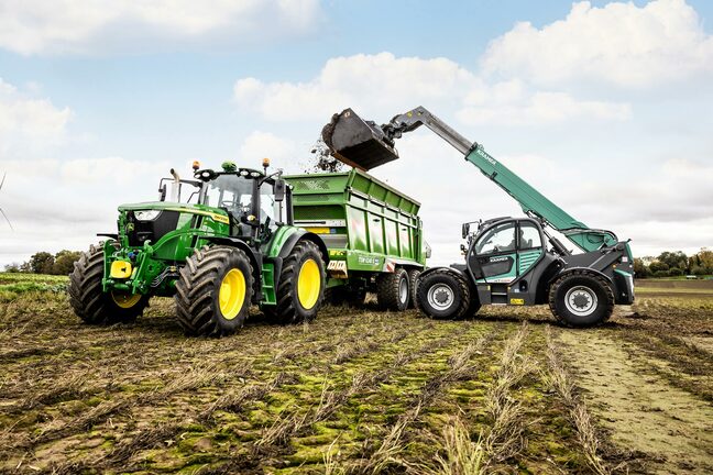 Un tractor John Deere încarcă o remorcă verde cu un încărcător telescopic în timpul lucrărilor la câmp