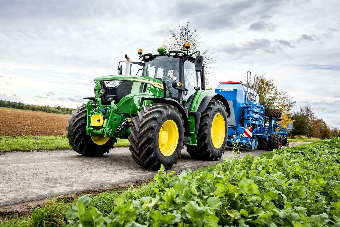 Un tractor John Deere trage o semănătoare de precizie de culoare albastră pe un drum de acces de la marginea culturilor