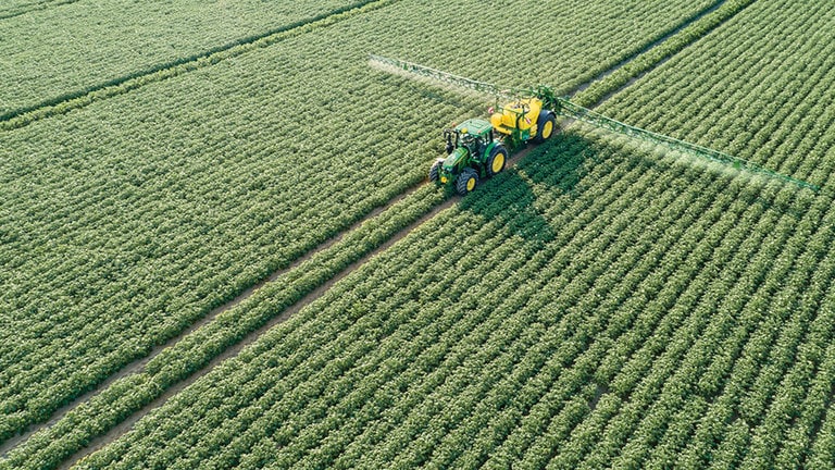 Tractor John Deere 6M Series care tractează o stropitoare M700 într-un câmp de cartofi