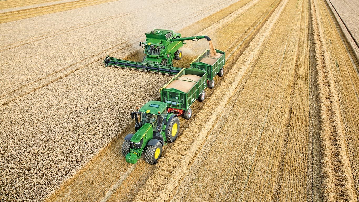 Combină John Deere Seria S descărcând grâu în trailele duale trase de tractor