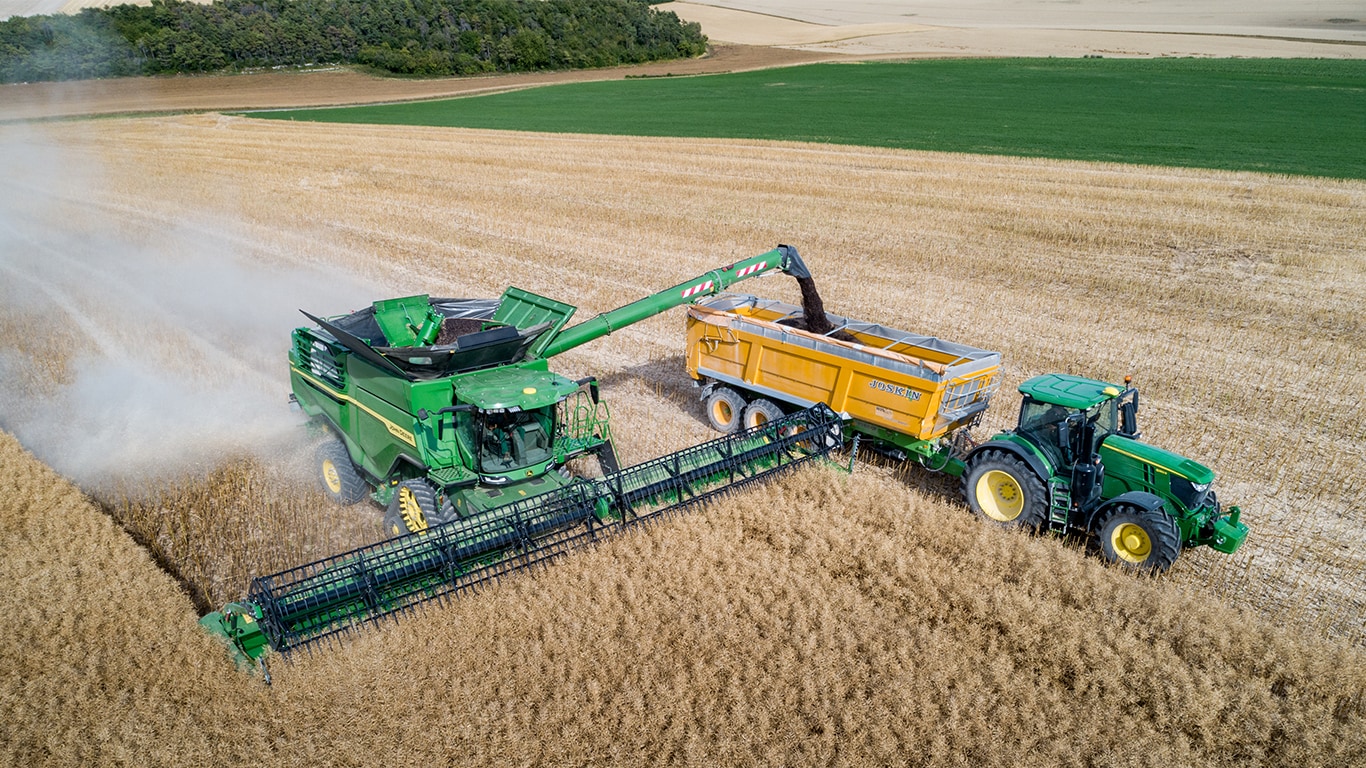Combină John Deere Seria S descărcând sămânţă de rapiţă într-o remorcă pentru grâne trasă de un tractor John Deere