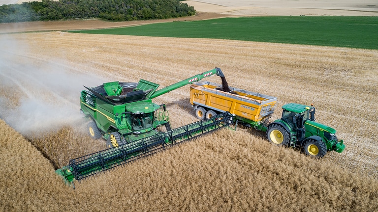 Combină John Deere Seria S descărcând sămânţă de rapiţă într-o remorcă pentru grâne trasă de un tractor John Deere
