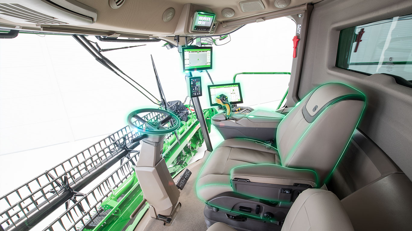 Interiorul cabinei combinei cu afişaje pentru agricultură de precizie, volan şi heder, vizibile prin parbriz