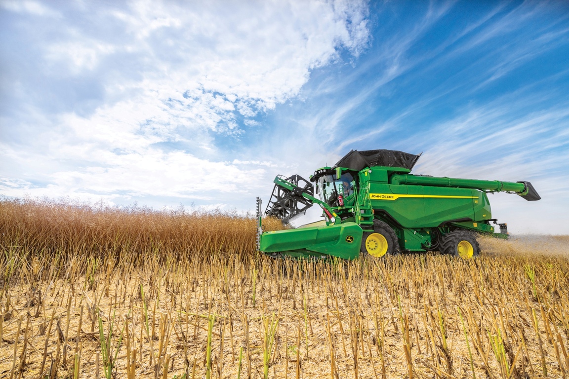 O combină John Deere recoltează boabe cu hederul, sub un cer senin, în plin sezon de recoltat