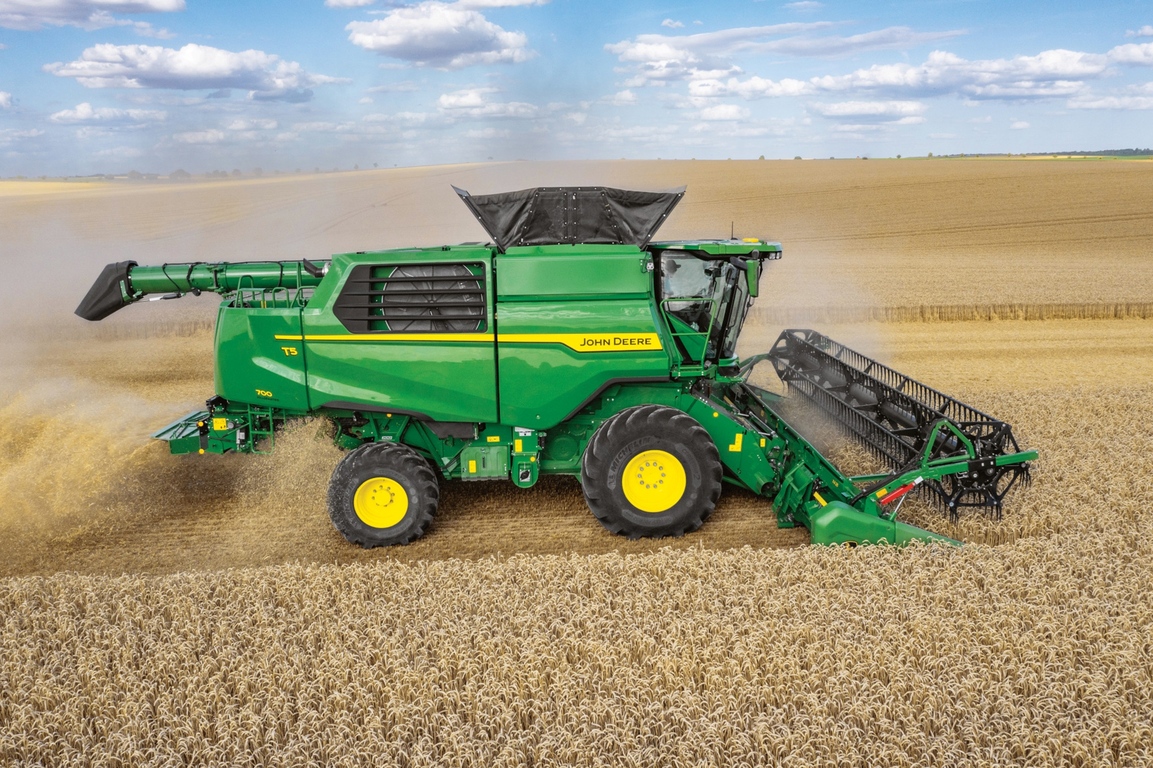 Vedere laterală a unei combine John Deere cu heder de tăiere care recoltează grâu pe un teren agricol întins