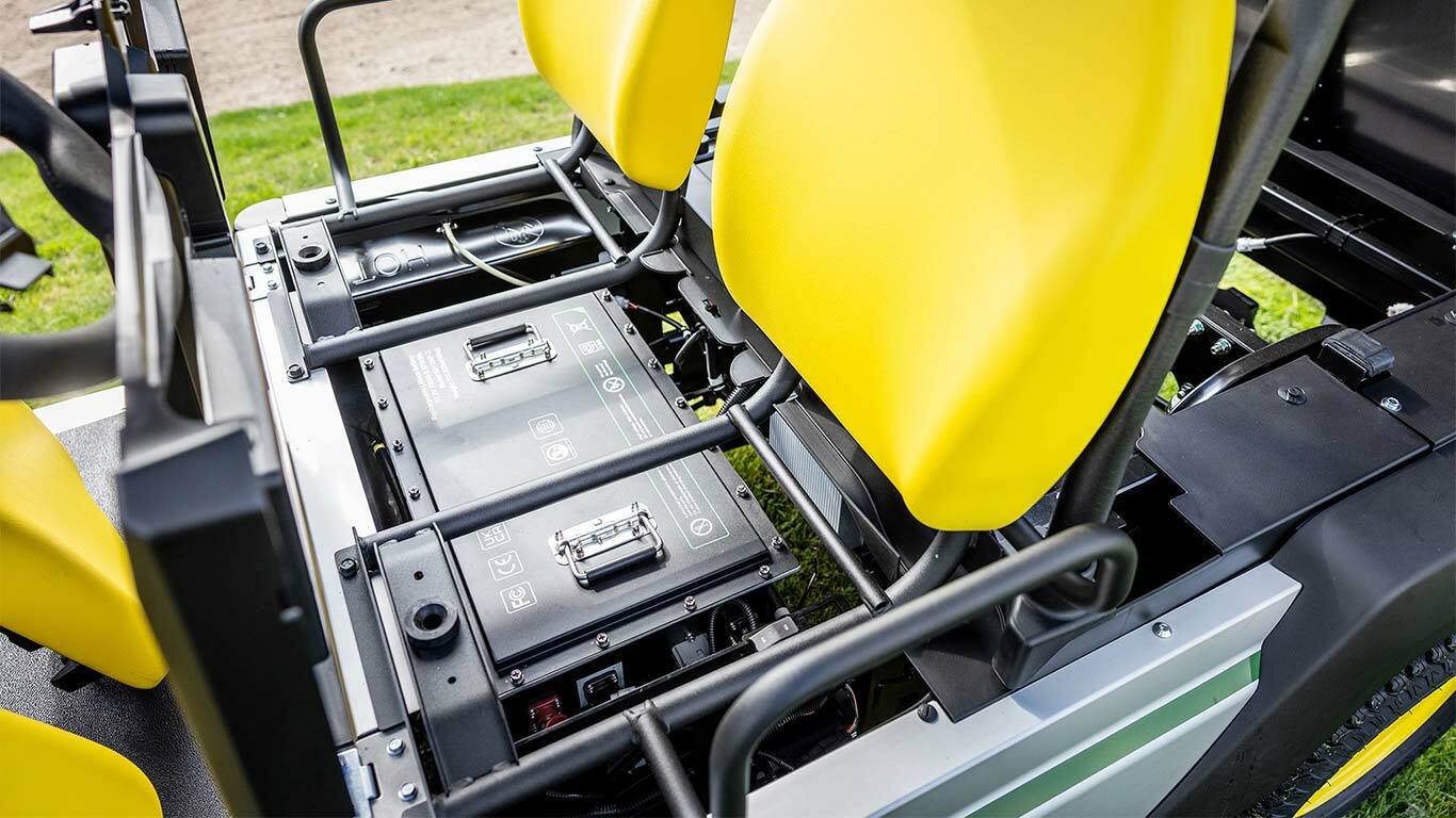 Prim-plan cu două baterii litiu instalate sub scaunele galbene ale unui vehicul utilitar electric John Deere Gator GS.