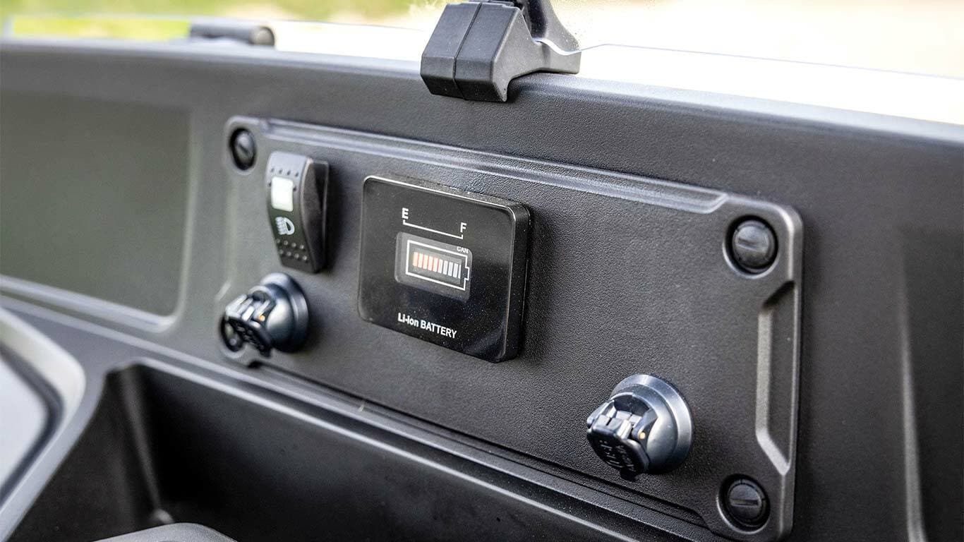 Tabloul de bord al modelului electric John Deere Gator GS, cu indicatorul stării bateriei şi prizele de alimentare vizibile.