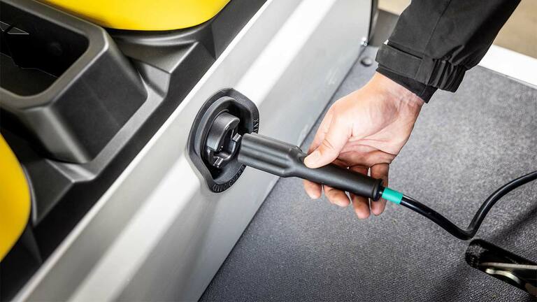 O mână introduce cablul de încărcare în portul lateral al unui vehicul utilitar electric John Deere Gator GS electric.