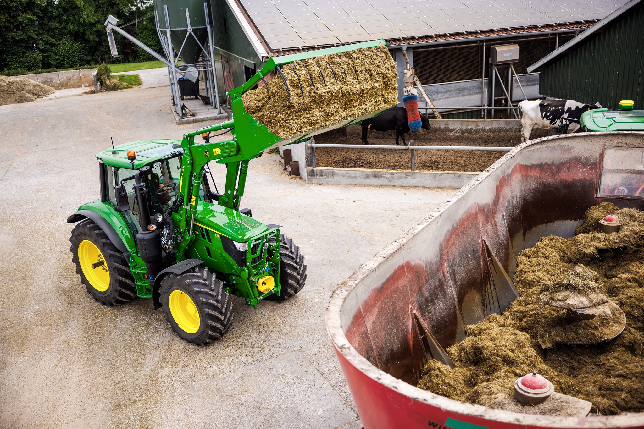 Tractor John Deere seria 6M cu încărcător frontal pentru alimentarea cu furaje a unui vagon cu mixer dintr-o fermă.