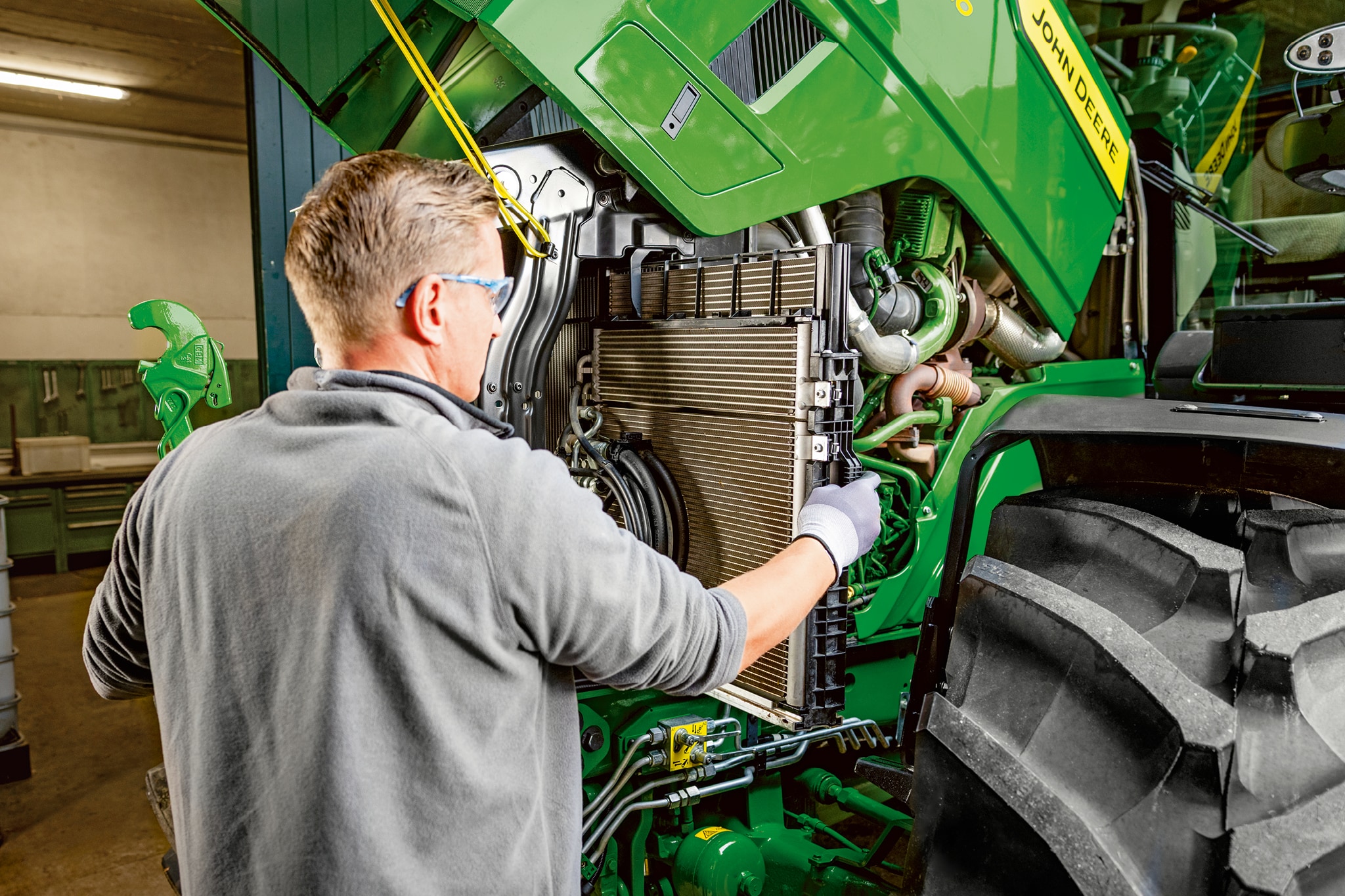 Un tehnician de service efectuează lucrări de întreţinere în compartimentul motor al unui tractor John Deere seria 6M.