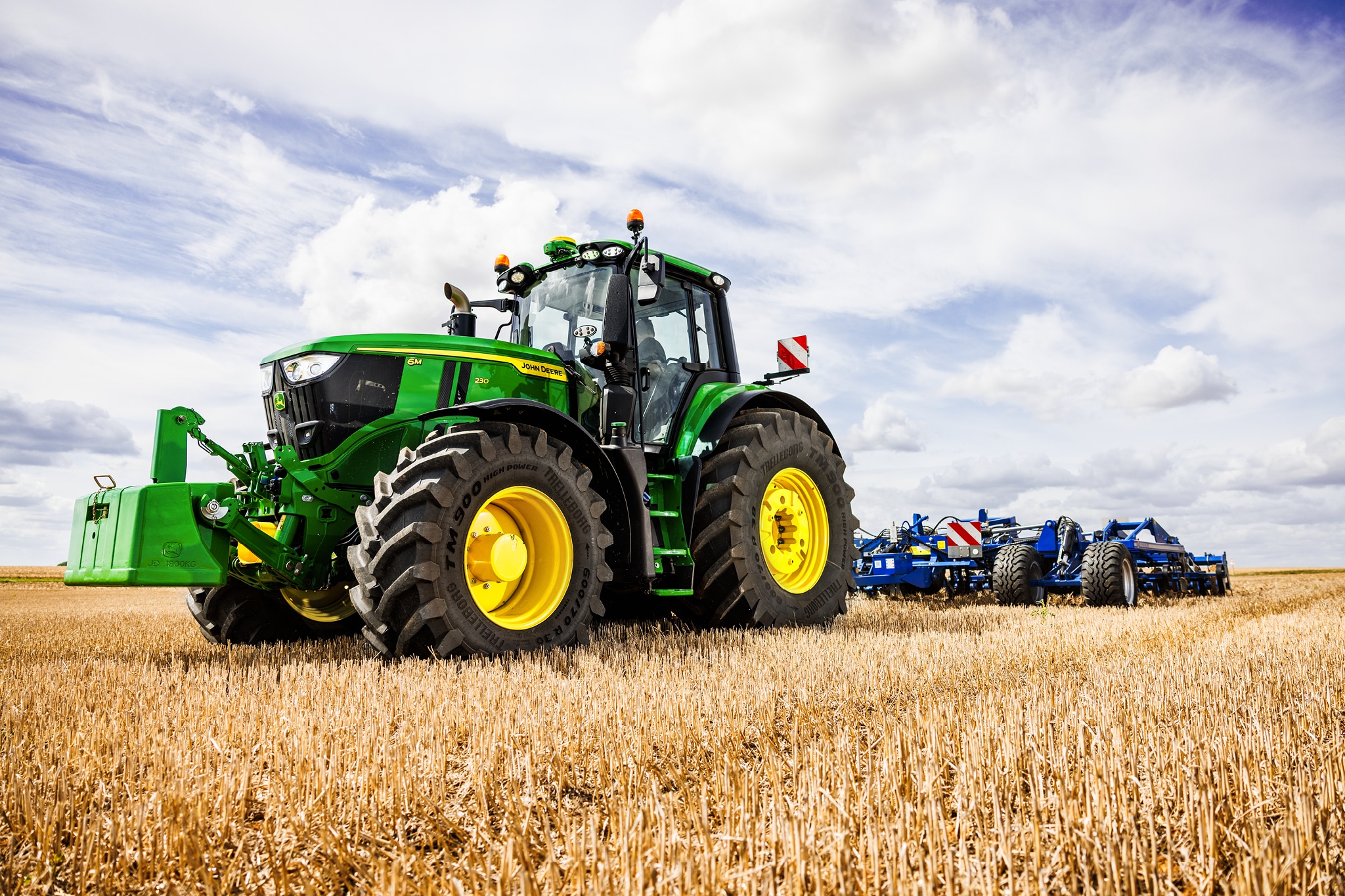 Tractorul John Deere seria 6M trage un instrument de arat greu peste o mirişte sub cerul înnorat.
