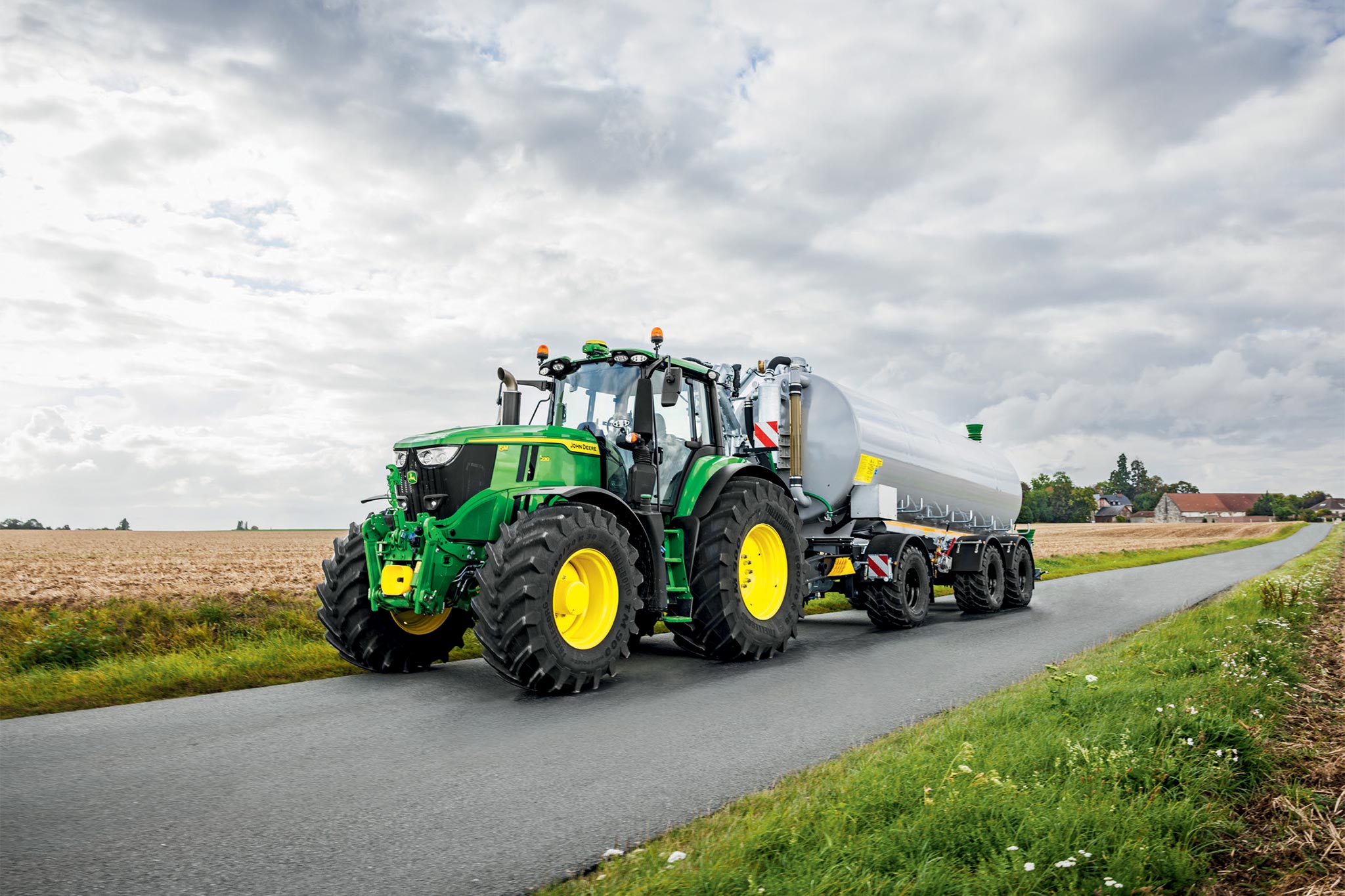 Tractor seria John Deere 6M pe un câmp recoltat cu cultivatoare late, privit de sus, cu praf ridicându-se în aer.