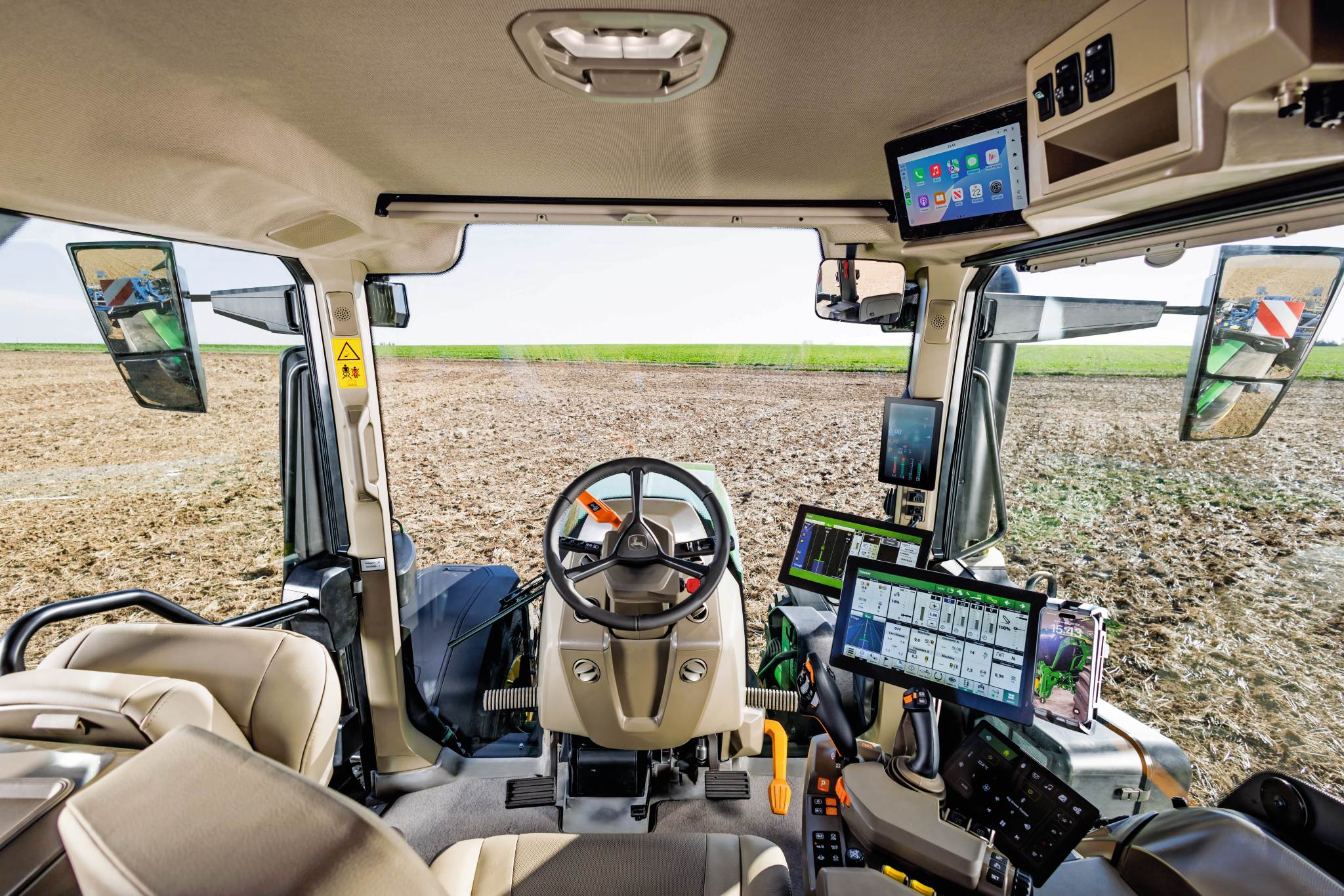 Interiorul modern al cabinei tractorului cu volan, afişaje cu ecran tactil şi comenzi pentru agricultură de precizie, cu vedere la un câmp cultivat