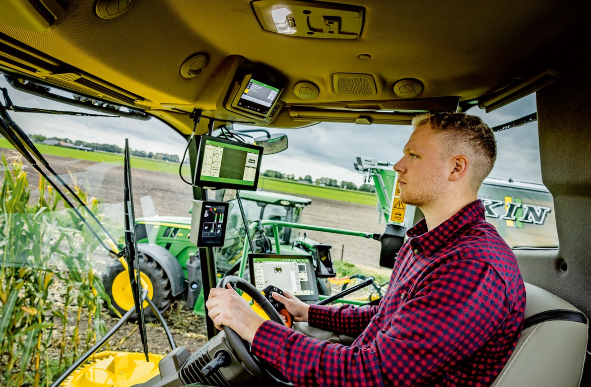 Fermier care utilizează utilaje agricole avansate cu mai multe ecrane digitale în cabina unei combine de furaje autopropulsate, cu tehnologie agricolă modernă pe un câmp.