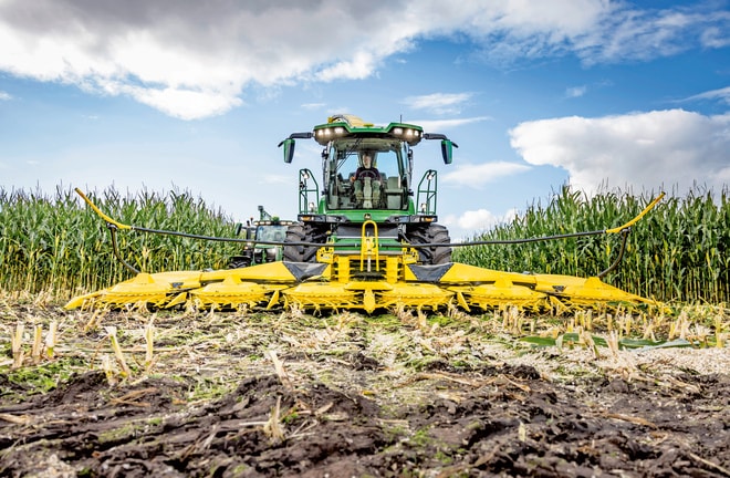 Utilaje agricole moderne, cu tehnologie şi echipamente agricole avansate, care recoltează porumb de pe câmp sub un cer parţial înnorat.