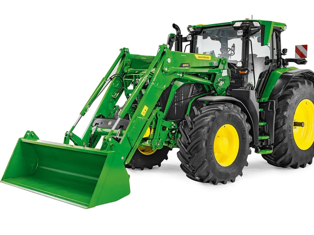 Tractor John Deere cu încărcător frontal şi cupă extinse, imagine în studio care evidenţiază raza de acţiune a încărcătorului şi înălţimea de ridicare.