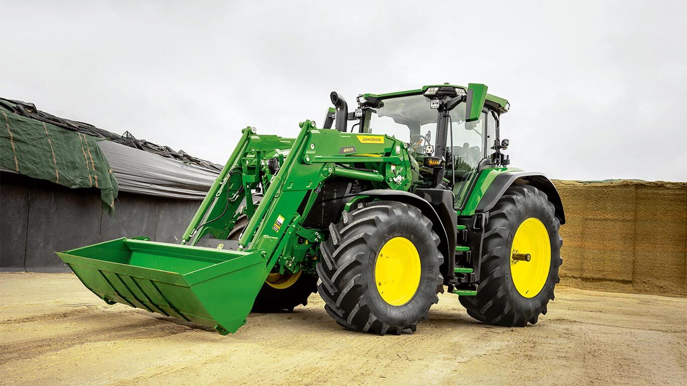 Tractor John Deere cu încărcător frontal parcat la fermă, lângă un depozit de furaje.