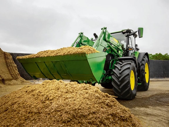 Tractor John Deere care utilizează încărcătorul frontal pentru a transporta furaje tăiate într-o zonă de depozitare agricolă.