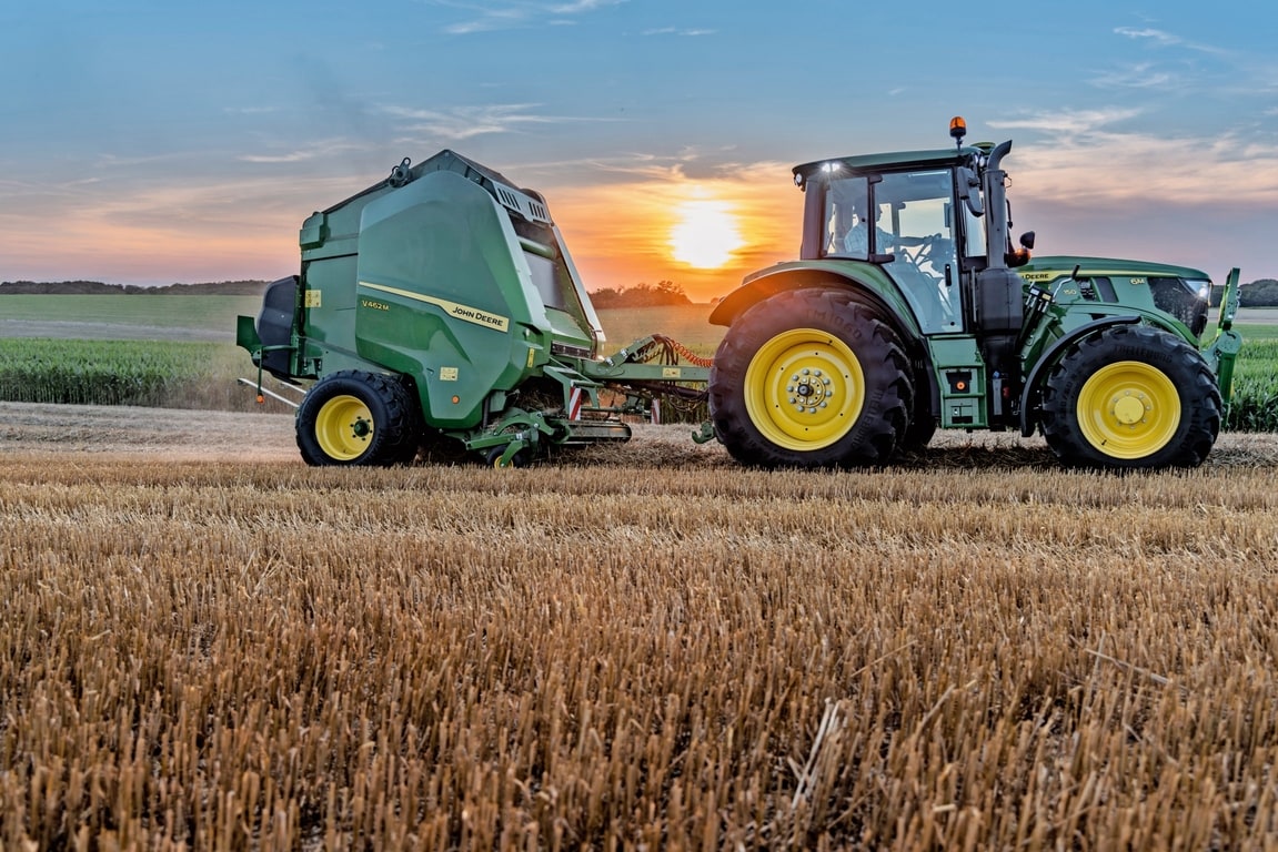 John Deere V462M pe un câmp de paie tras de un John Deere 6M 150 la apus