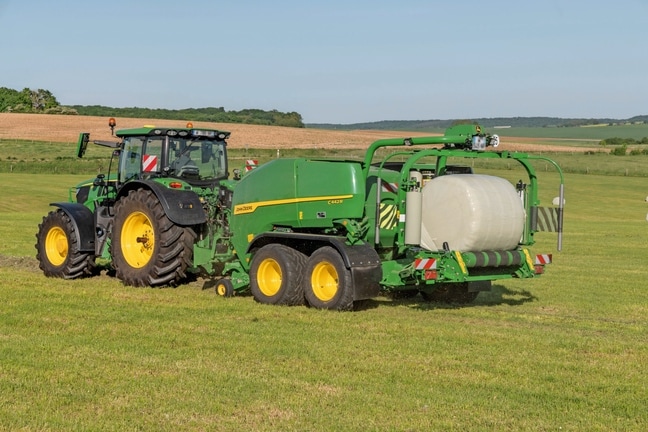 Presă de balotat cu sistem de înfoliere John Deere C442R trasă de un John Deere 6R 185 care realizează baloţi de furaje de mare densitate