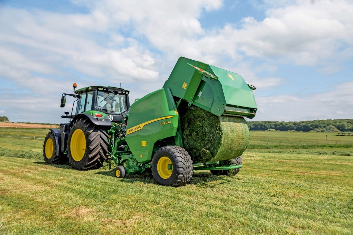 Presă de balotat John Deere F442M trasă de un tractor John Deere 6M în timp ce ejectează un balot de iarbă