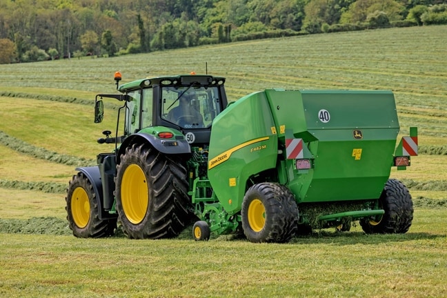 Presa de balotat John Deere F442M trasă de un tractor John Deere 6M pe un câmp deluros cu iarbă