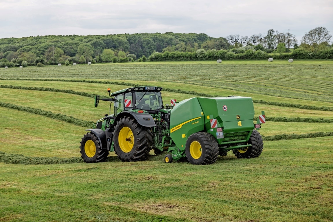 Presa de balotat John Deere F442R trasă de un tractor John Deere 6M pe un câmp deluros cu iarbă