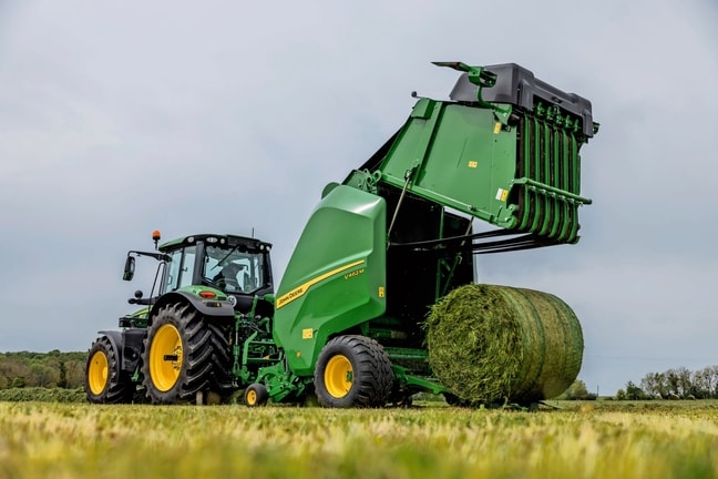 Presă de balotat John Deere V462M trasă de un tractor John Deere 6M în timp ce ejectează un balot de iarbă
